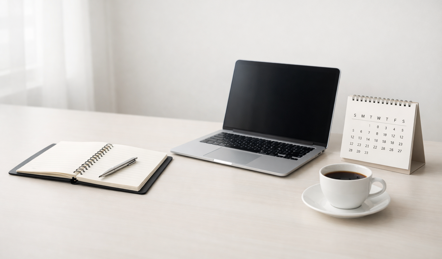 A clean, minimal workspace with a laptop, notebook, and calendar arranged neatly on a desk.